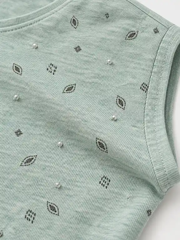 Close-up of small light-toned hand-sewn beads and dark leaf prints on mint green jersey