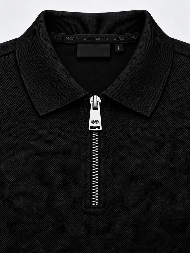 Detail of a black flat-knit polo collar with integral knitted edge and a metal zipper with logo lettering on the pull