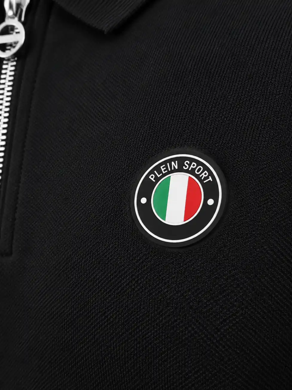 Close-up of a separately made circular silicone chest badge with light outlines, lettering and green white red center on a black polo shirt