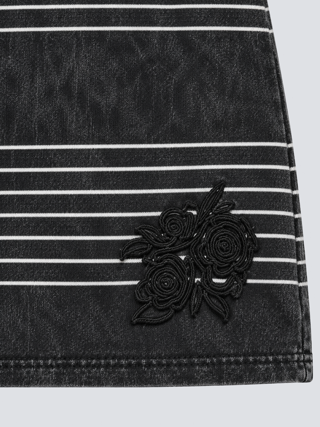 Hand-sewn black self-fabric flower at right front hem